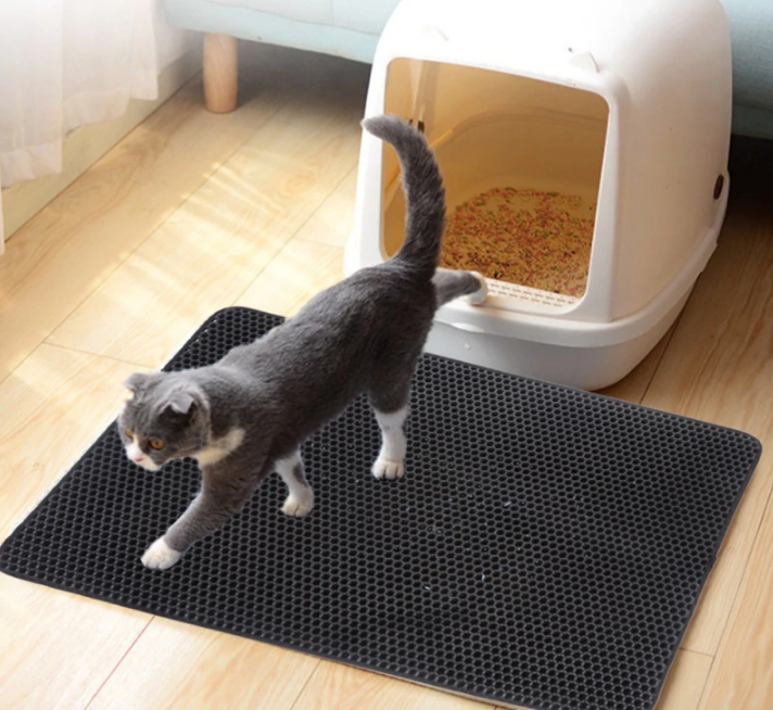 Double-layer honeycomb cat litter trapping mat in black on floor next to litter box
